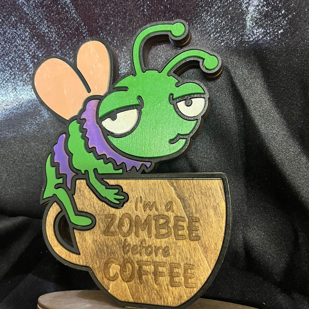 Wooden figurine of a green insect character on a coffee cup with 'I'm a zombee before coffee text.