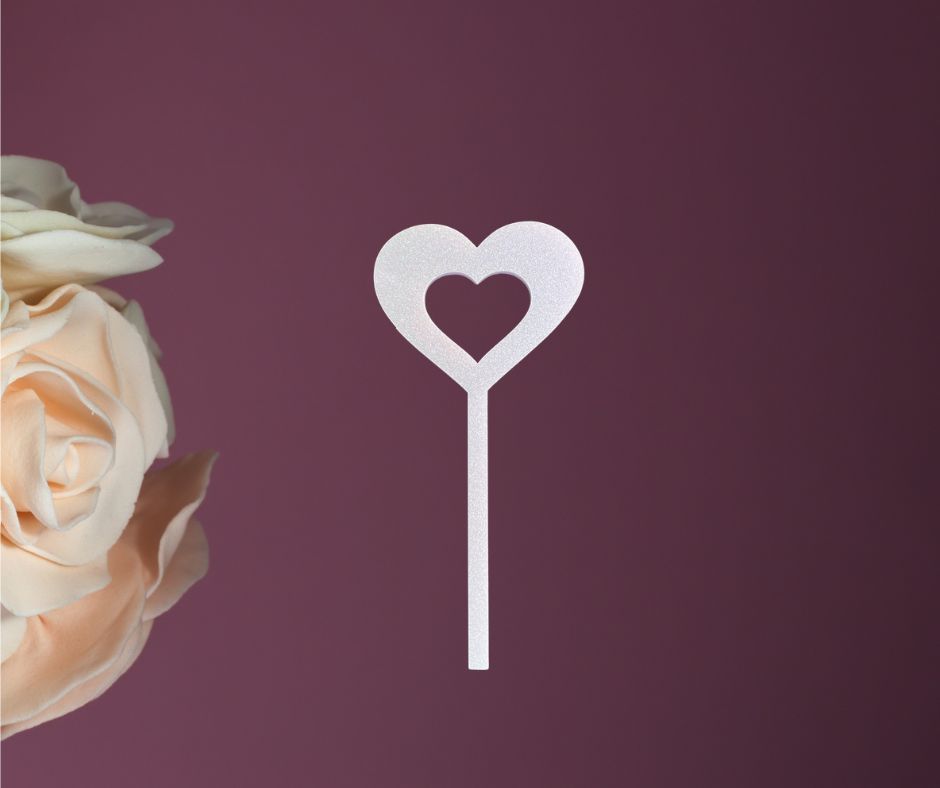 Heart-shaped cake topper next to a rose on a purple background