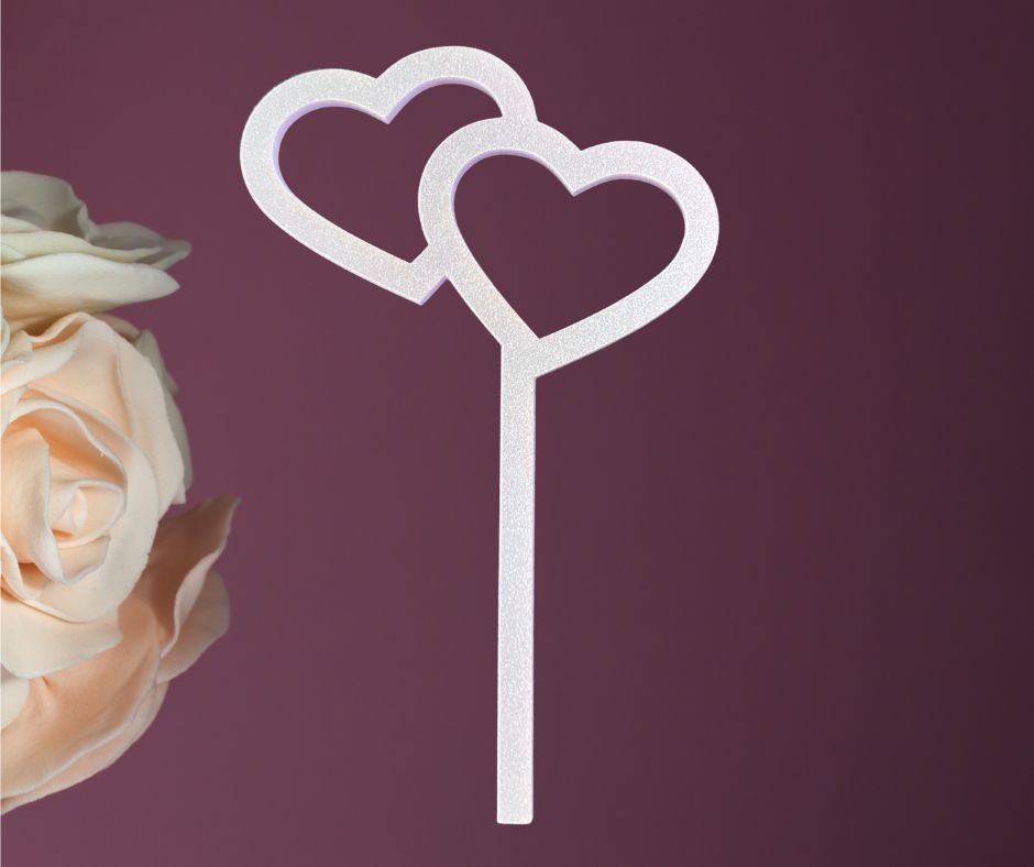 Two heart-shaped cake toppers on a stick with a rose on a purple background