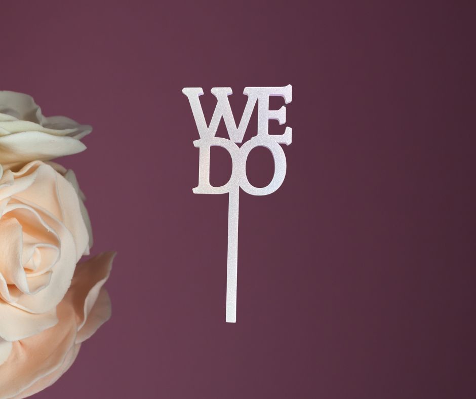 Wedding cake topper with 'WE DO' on a purple background with roses.