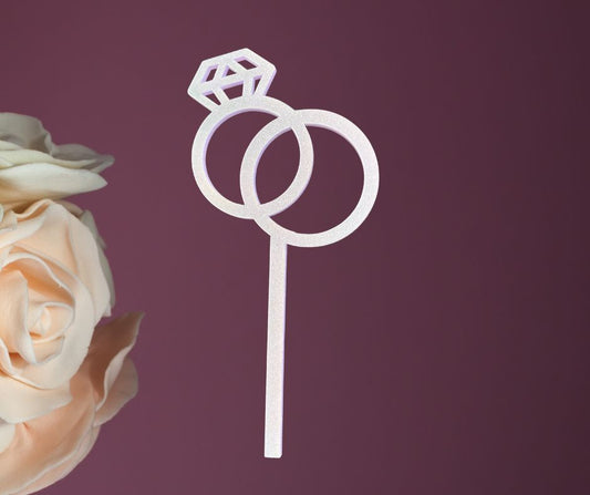 Decorative cake topper with two interlocking rings and a diamond on a purple background with a rose.